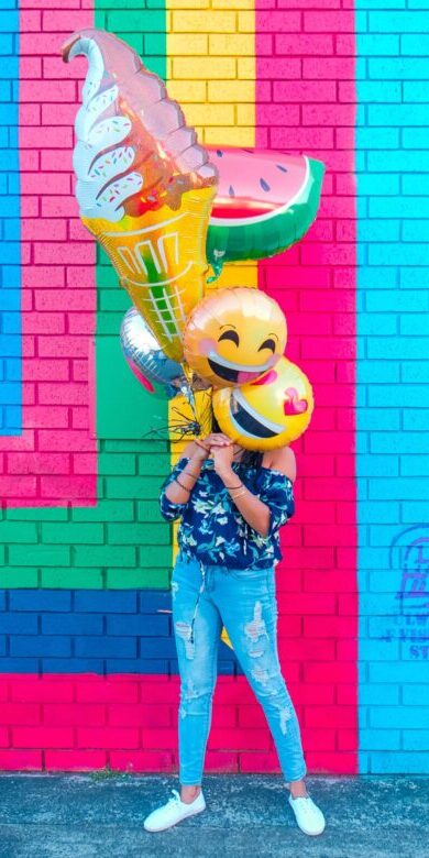 A woman holding a group of cute balloons over her face.